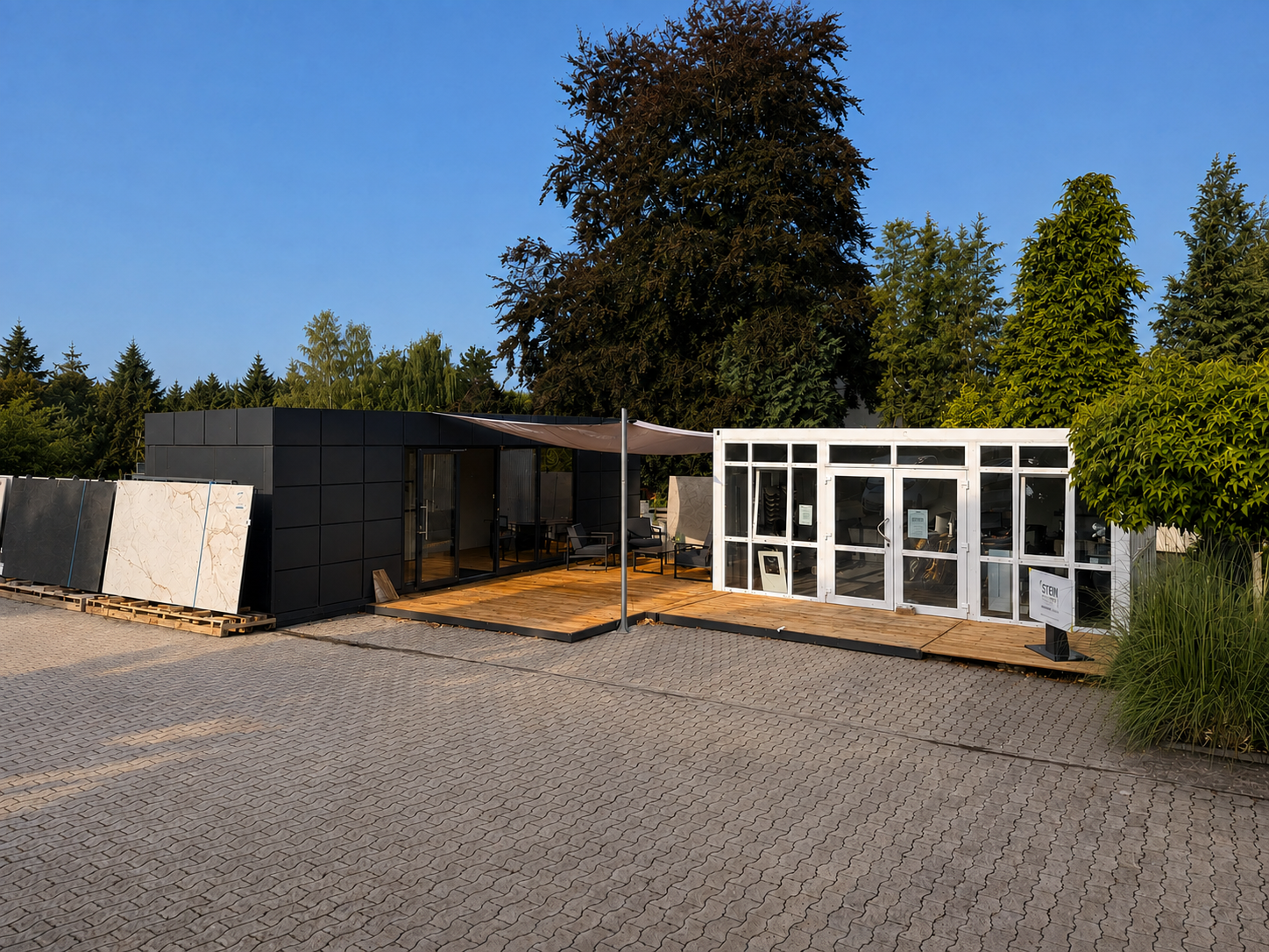Außenansicht von STEINFORMAT mit Materialplatten, Terrasse und gläsernem Eingang; Hintergrund und Licht bearbeitet, Perspektive korrigiert