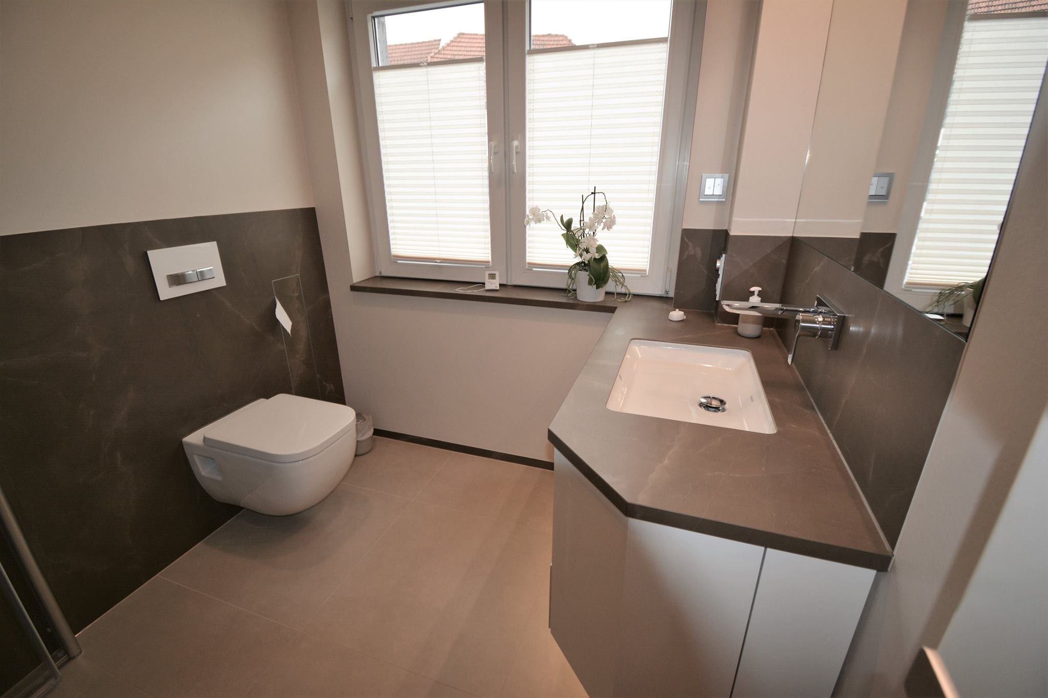 Braungraue Waschtischplatte mit weißem Unterbaubecken, abgeschrägter Ecke und passender Rückwand