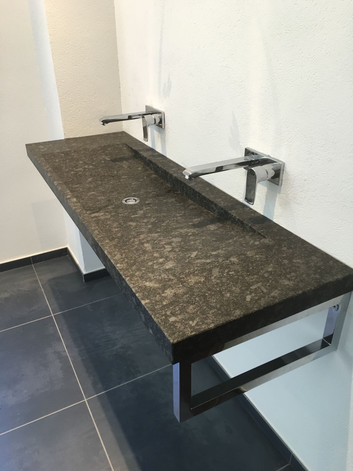 Langer dunkler Waschtisch mit flachem Becken, zwei Wandarmaturen und offenem Metallgestell