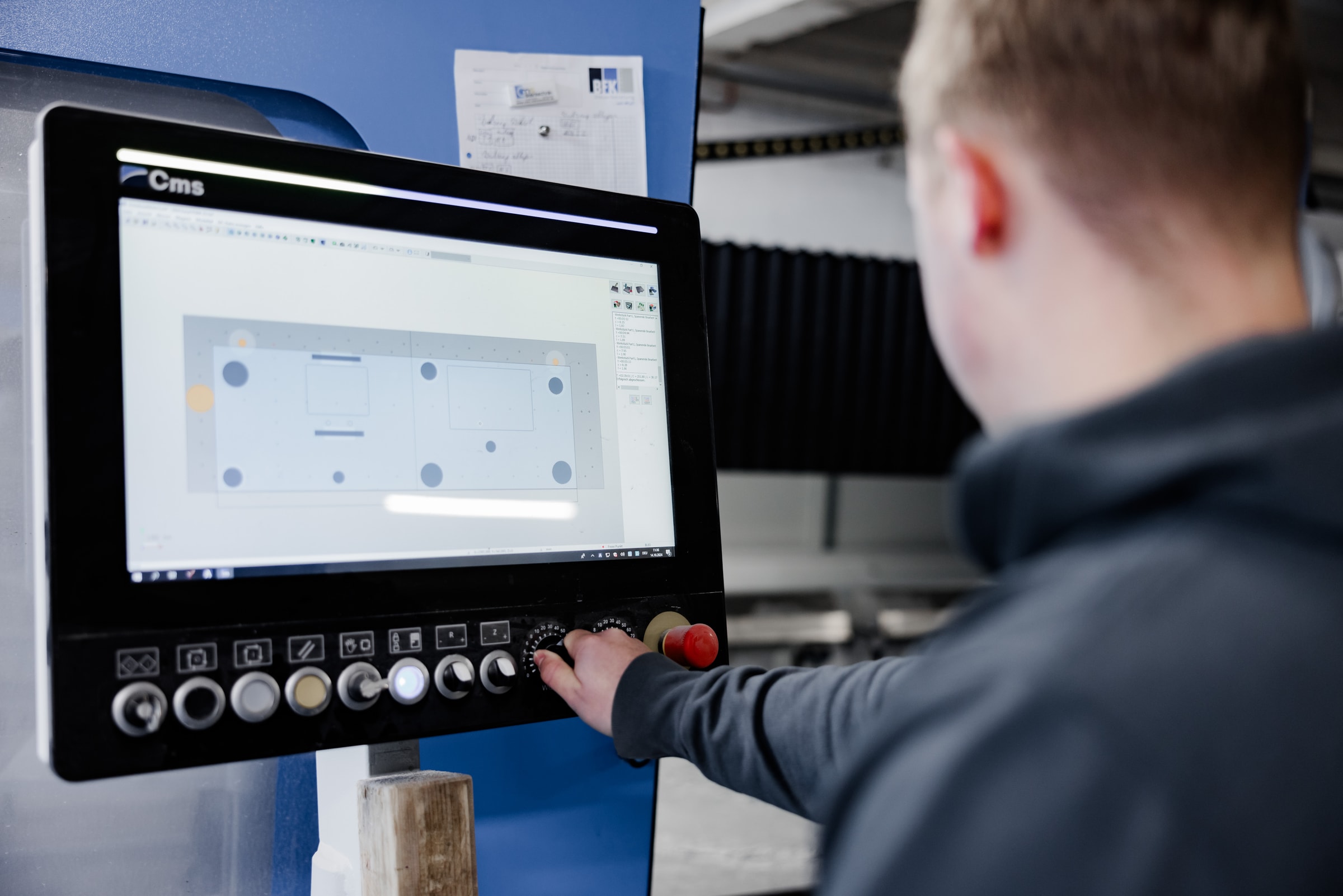 Mitarbeiter bedient die CNC-Steuerung mit einer Werkstückzeichnung auf dem Bildschirm